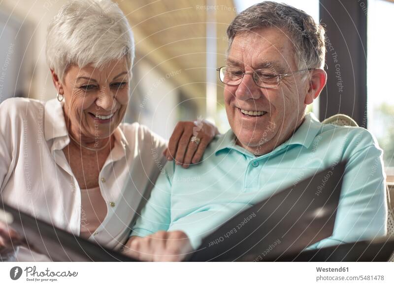 Glückliches älteres Paar sitzt auf der Couch und schaut sich ein Fotoalbum an Sofa Couches Liege Sofas ansehen glücklich glücklich sein glücklichsein Zuhause