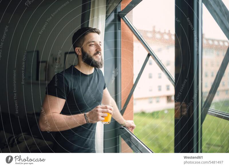 Junger Mann trinkt einen Orangensaft am Fenster Saft Saefte Säfte lächeln trinken Männer männlich Getränk Getraenk Getränke Getraenke Food and Drink