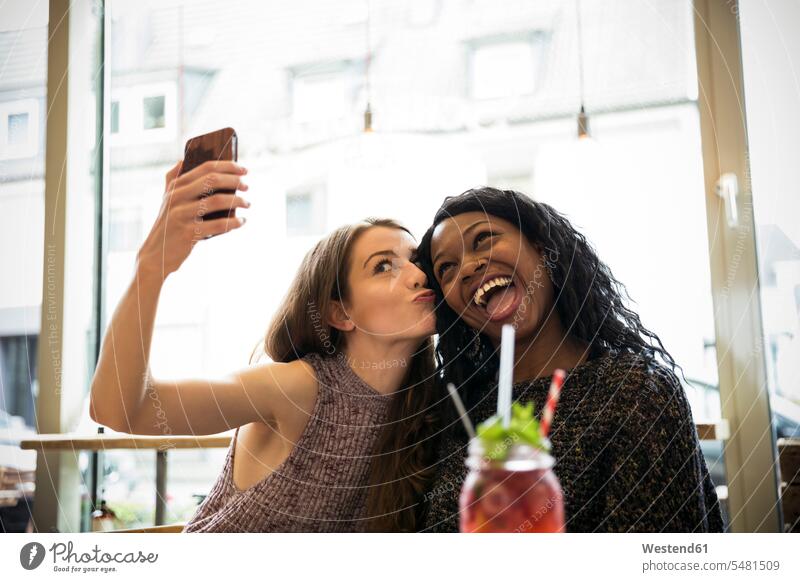 Zwei junge Frauen machen ein Selfie in einem Cafe Freundinnen Treffen Begegnung Spaß Spass Späße spassig Spässe spaßig Gemeinsam Zusammen Miteinander Selfies