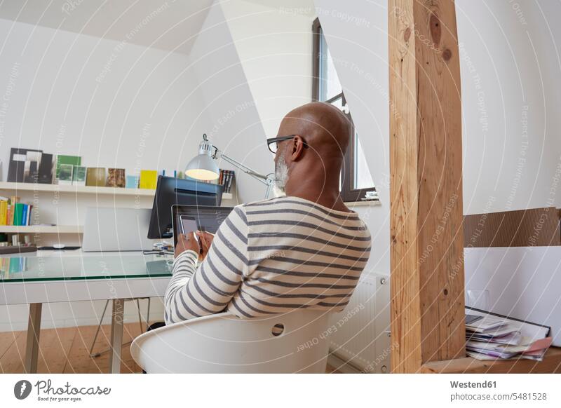 Rückenansicht eines Mannes, der am Schreibtisch seines Heimbüros sitzt und ein Smartphone benutzt Afroamerikanisch Afro-Amerikanisch Afroamerikaner