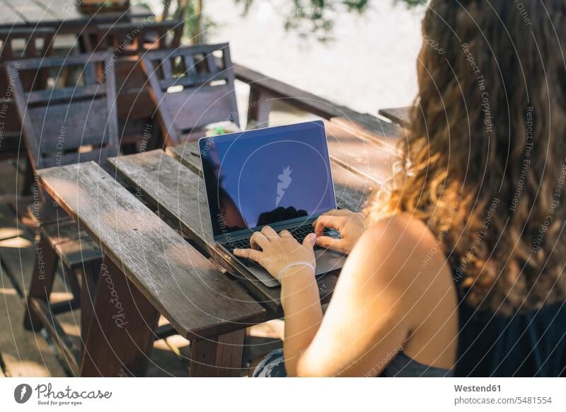 Junge Frau sitzt im Freien und benutzt einen Laptop Tisch Tische arbeiten Arbeit sitzen sitzend schreiben aufschreiben notieren schreibend Schrift Urlaub Ferien