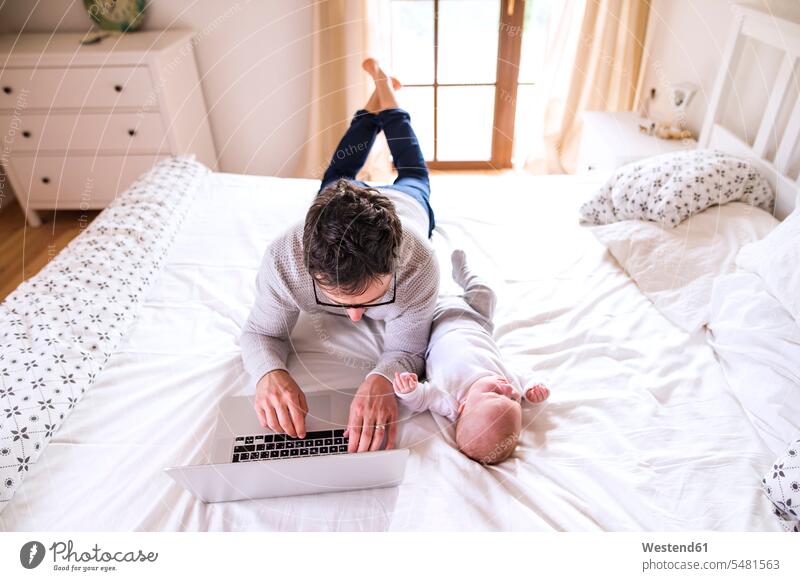 Vater mit Baby auf dem Bett liegend mit Laptop Notebook Laptops Notebooks Papas Väter Vati Vatis Papis Kind Kinder Babies Babys Computer Rechner Eltern Familie