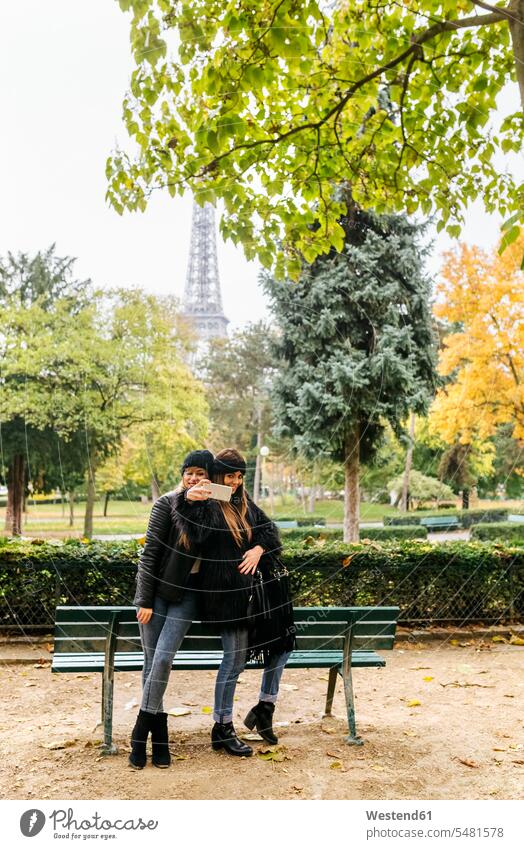 Frankreich, Paris, zwei junge Frauen machen ein Selfie im Park mit dem Eiffelturm im Hintergrund Freundinnen Selfies Parkanlagen Parks lächeln Handy