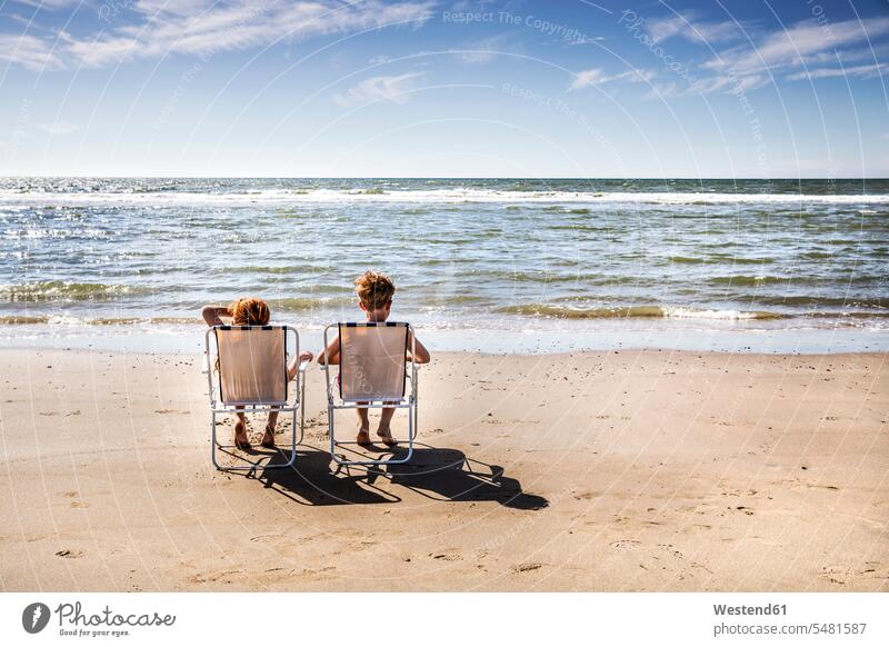 Niederlande, Zandvoort, Junge und Mädchen sitzen auf Stühlen am Strand Beach Straende Strände Beaches weiblich sitzend sitzt Buben Knabe Jungen Knaben männlich