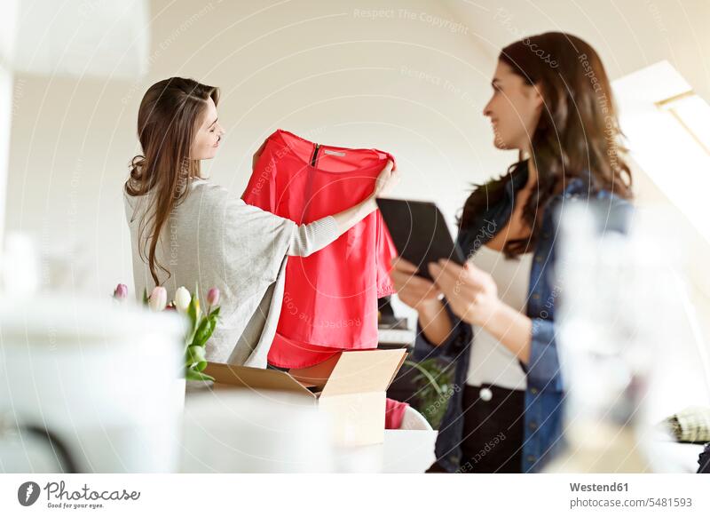 Zwei Frauen mit digitalem Tablett und Päckchen mit Kleidungsstück Freundinnen auspacken lächeln Tablet Computer Tablet-PC Tablet PC iPad Tablet-Computer Kleider