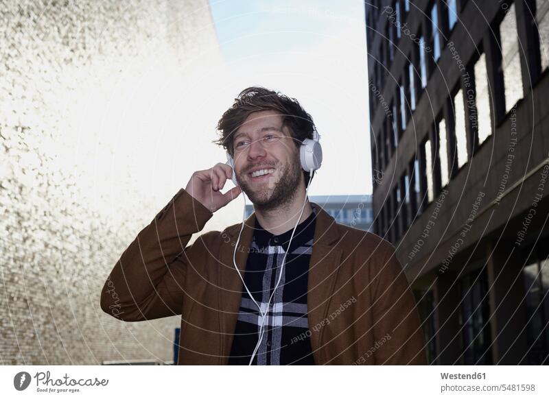 Lächelnder junger Mann hört Musik mit Kopfhörern im Gegenlicht Europäer Kaukasier Europäisch kaukasisch braune Haare braunhaarig brünett braunes Haar