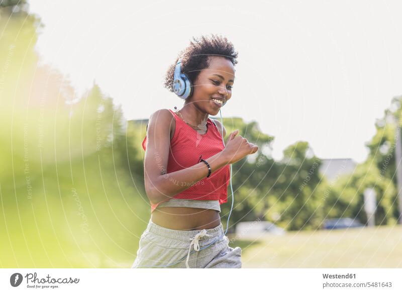 Junge Frau mit Kopfhörern läuft im Park lächeln laufen rennen Parkanlagen Parks Joggen Jogging Kopfhoerer trainieren weiblich Frauen Fitness fit Gesundheit