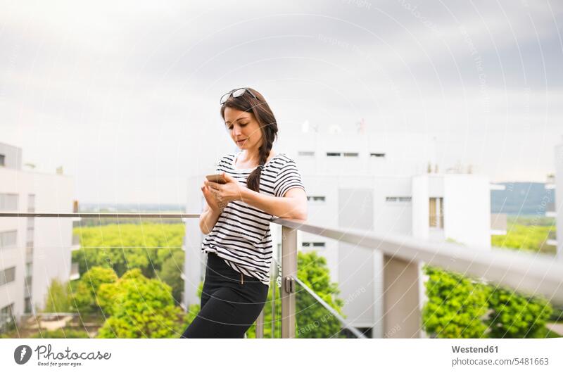 Frau benutzt Smartphone auf dem Balkon weiblich Frauen Balkone Dachterrasse Dachterrassen Erwachsener erwachsen Mensch Menschen Leute People Personen Terrasse