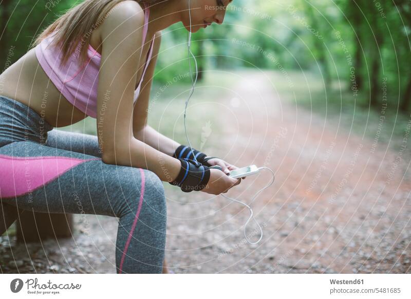 Sportliche Frau macht Pause im Wald Forst Wälder sportlich trainieren Handy Mobiltelefon Handies Handys Mobiltelefone weiblich Frauen sitzen sitzend sitzt