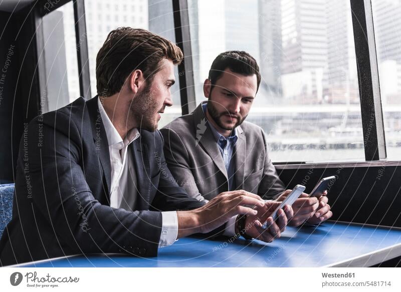 Zwei Geschäftsleute mit Mobiltelefonen im Gespräch auf dem Passagierdeck einer Fähre Geschäftsmann Businessmann Businessmänner Geschäftsmänner sprechen reden