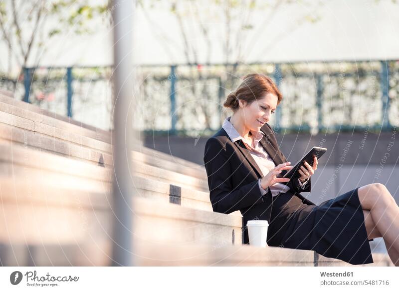 Geschäftsfrau sitzt auf einer Treppe und benutzt ein Tablett Geschäftsfrauen Businesswomen Businessfrauen Businesswoman Treppenaufgang Tablet Computer Tablet-PC