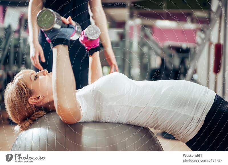 Schwangere Frau macht Übungen mit Handgriffen auf Fitnessball im Fitness-Studio Gymnastikball Sitzball weibliche Erwachsene Frauen Handhantel Hantel Hanteln