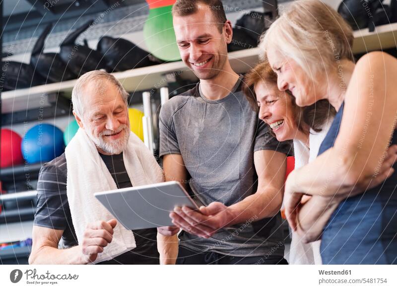Gruppe von fitten Senioren und Personal Trainer im Fitnessstudio betrachtet Tablette Fitnessclubs Fitnessstudios Turnhalle Tablet Computer Tablet-PC Tablet PC