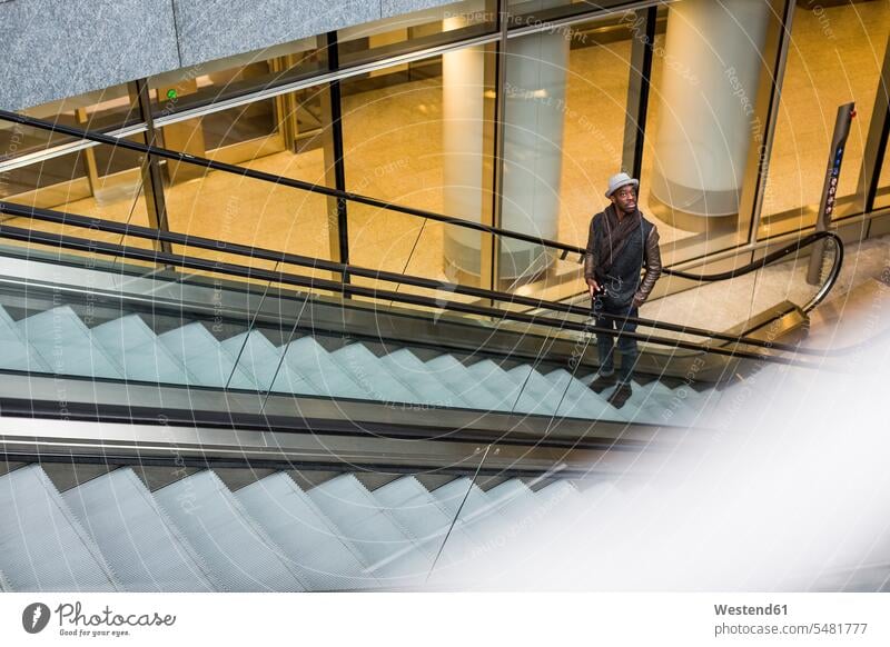 Junger Mann steht auf Rolltreppe und schaut sich um Fahrtreppe Männer männlich Erwachsener erwachsen Mensch Menschen Leute People Personen stehen stehend Handy