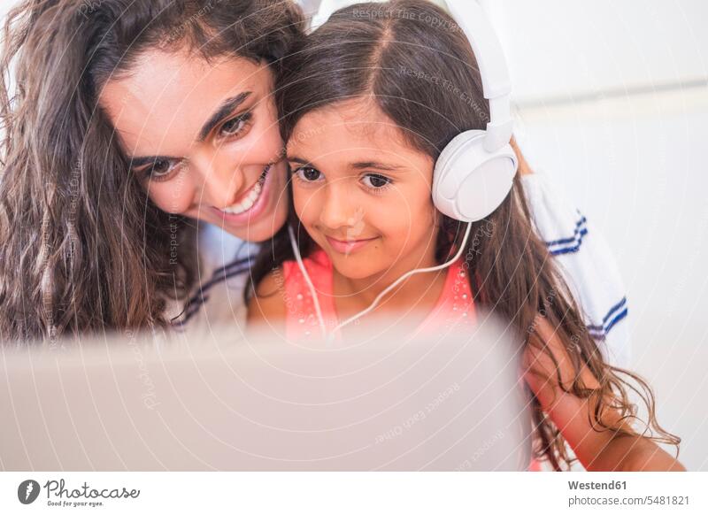 Glückliche Teenagerin und ihre kleine Schwester mit Laptop und Kopfhörern Mädchen weiblich Kopfhoerer Schwestern lächeln glücklich glücklich sein glücklichsein