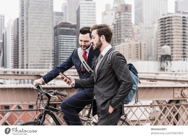 USA, New York City, zwei Geschäftsleute mit Fahrrad und Handy auf der Brooklyn Bridge sprechen reden New York State Geschäftsmann Businessmann Businessmänner