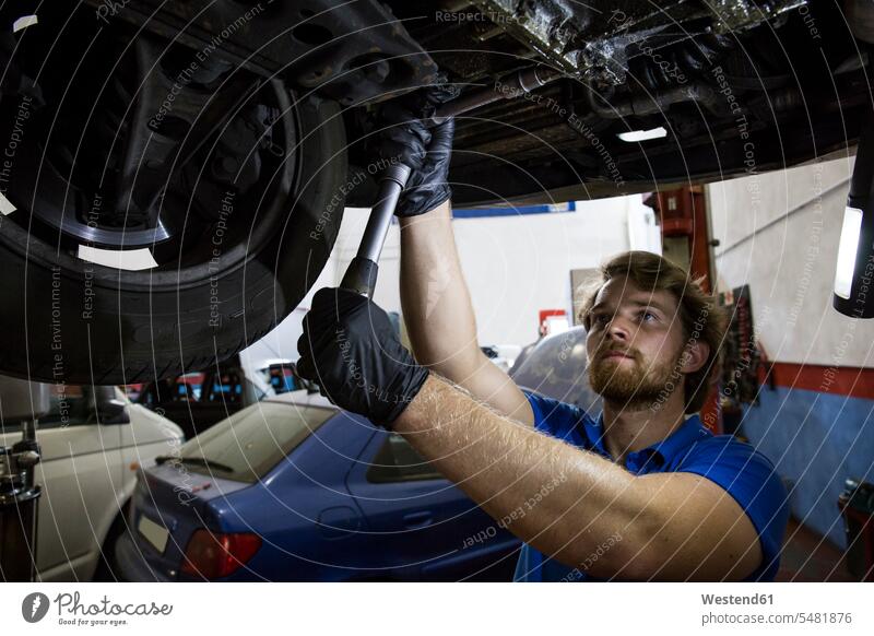 Mechaniker, der in seiner Werkstatt ein hängendes Auto repariert Monteur Schraubenschlüssel Hebebühne Hebebühnen Kfz-Werkstatt Kfz-Werkstaetten Autowerkstatt