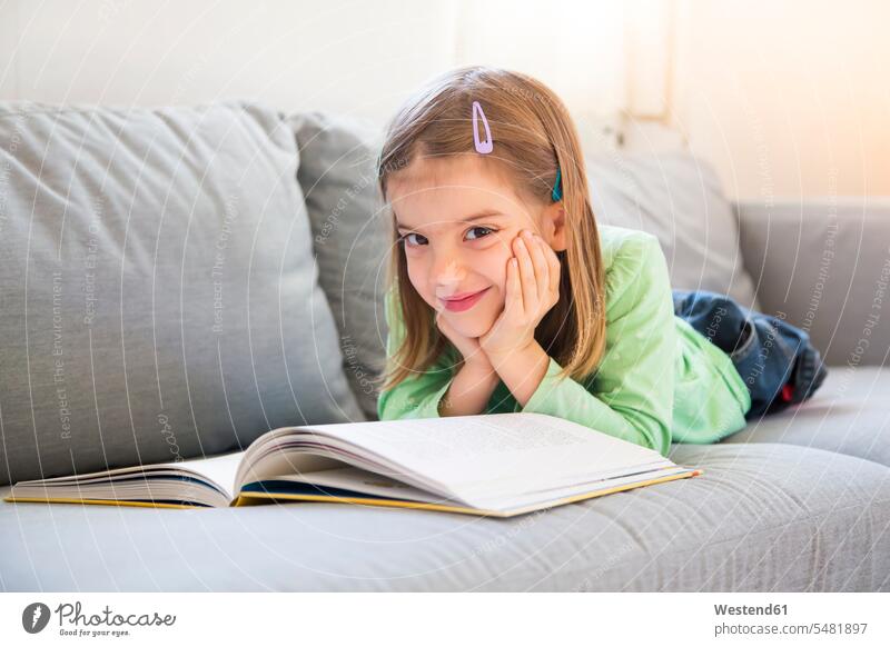 Porträt eines lächelnden kleinen Mädchens, das mit einem Buch auf der Couch liegt weiblich Bücher Portrait Porträts Portraits Kind Kinder Kids Mensch Menschen