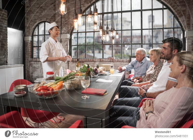 Gruppe von Personen, die an einem Kochkurs teilnehmen erklären kochen Köchin Zutaten Gemüse lernen Gastronomie Essen Food and Drink zuhören Freude sitzen