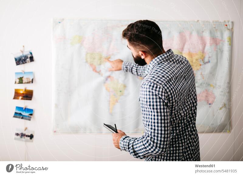 Junger Mann wählt Reiseziele auf einer Weltkarte aus Europäer Kaukasier Europäisch kaukasisch Freizeitkleidung casual Freizeitbekleidung Oberkörper