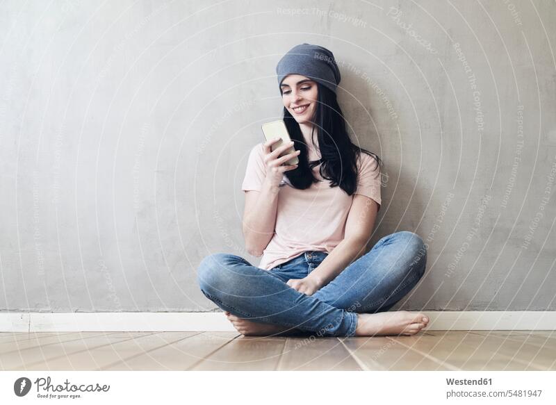 Lächelnde junge Frau sitzt auf dem Boden und benutzt ein Mobiltelefon Handy Handies Handys Mobiltelefone lächeln weiblich Frauen sitzen sitzend Telefon