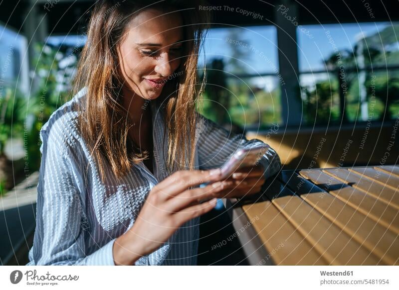 Lächelnde Frau auf der Terrasse, die auf ihr Handy schaut weiblich Frauen Terrassen Smartphone iPhone Smartphones Erwachsener erwachsen Mensch Menschen Leute