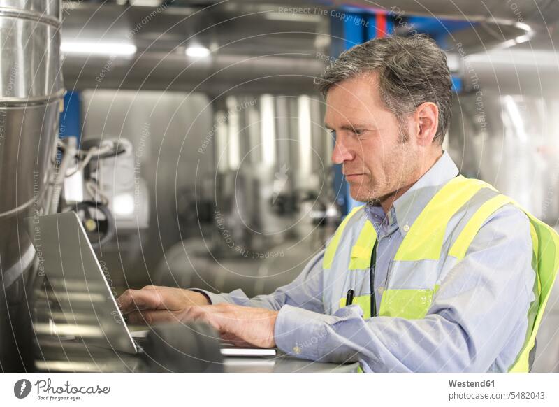 Mann trägt reflektierende Weste mit Laptop in einer Industrieanlage Fabrik Fabrikgebäude Fabrikgebaeude Fabriken Verbindung verbunden verbinden Anschluss