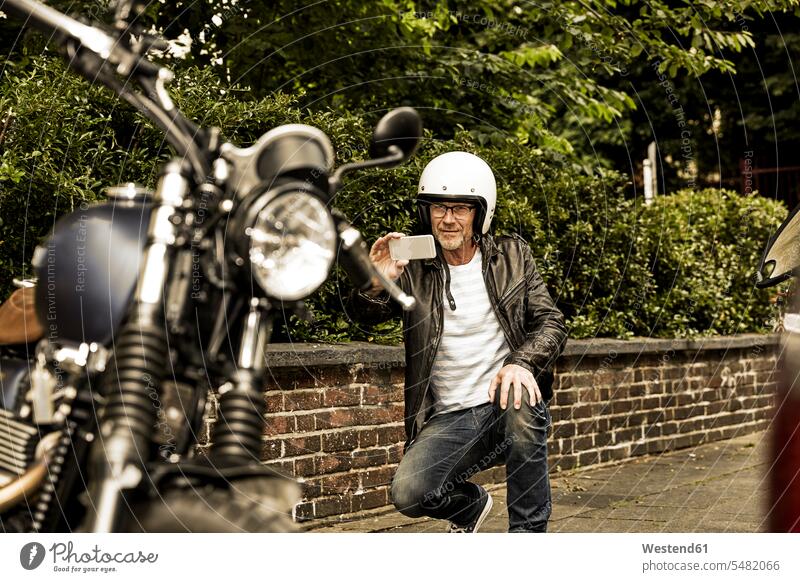 Lächelnder Mann mit Motorradhelm beim Fotografieren seines Motorrads Männer männlich fotografieren Erwachsener erwachsen Mensch Menschen Leute People Personen
