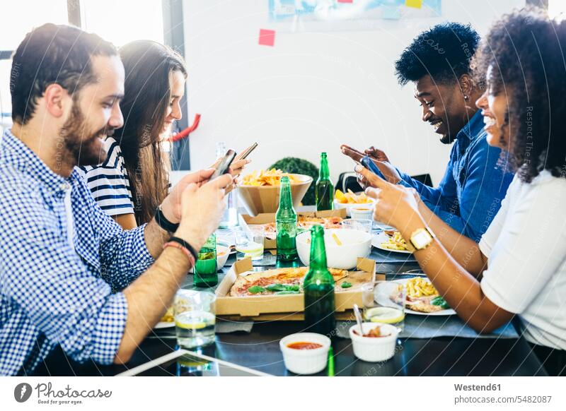 Freunde benutzen Mobiltelefone am Esstisch Tisch Tische Handy Handies Handys essen essend Freundschaft Kameradschaft Telefon telefonieren Kommunikation