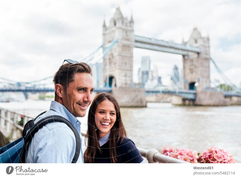 UK, London, lächelndes Paar mit der Tower Bridge im Hintergrund Pärchen Paare Partnerschaft England Großbritannien Vereinigtes Königreich Mensch Menschen Leute