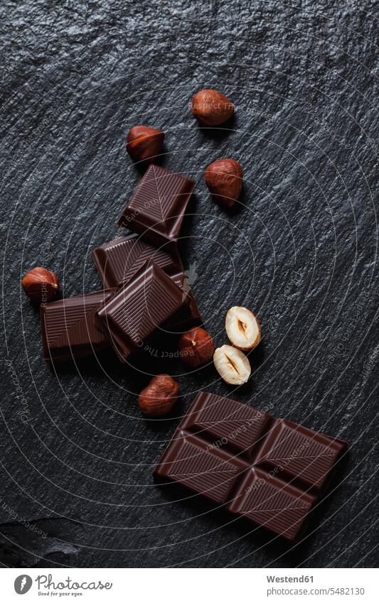 Zartbitterschokolade und Haselnüsse auf Schiefer schwarzer Hintergrund Gruppierung Anordnung Ordnung gruppiert gruppieren Schokoladentafel Tafel Schokolade