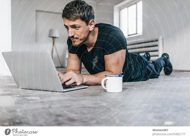Auf dem Boden liegender Mann mit Laptop im leeren Dachboden Notebook Laptops Notebooks liegt Männer männlich Computer Rechner Erwachsener erwachsen Mensch