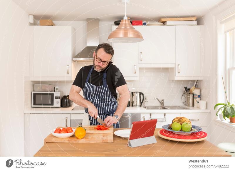 Mann telefoniert mit Smartphone, während er in der Küche Gemüse zubereitet zuhören zuhörend Food and Drink Lebensmittel Essen und Trinken Nahrungsmittel Paprika