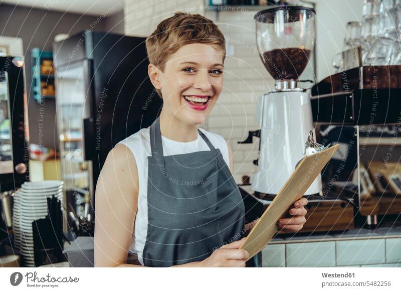 Porträt einer lachenden Kellnerin, die in einem Cafe die Speisekarte hält Restaurantfachfrau Kellnerinnen Kaffeehaus Bistro Cafes Café Cafés Kaffeehäuser Frau