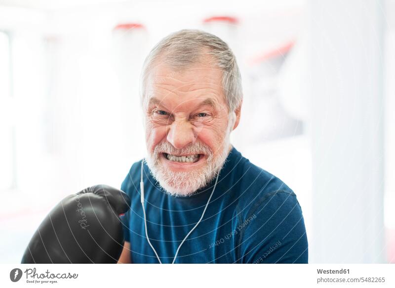 Porträt eines aggressiven älteren Mannes mit Kopfhörern und Boxhandschuhen im Fitnessstudio Fitnessclubs Fitnessstudios Turnhalle Senior ältere Männer