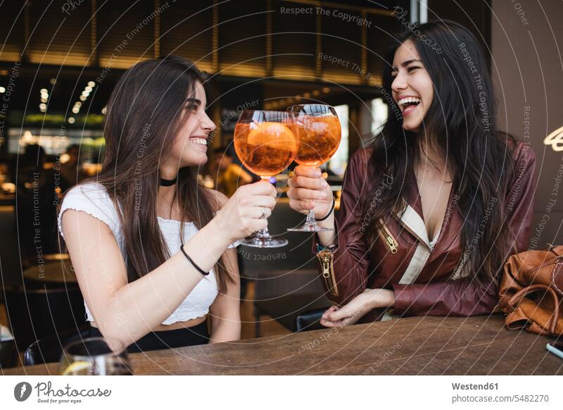 Zwei glückliche junge Frauen stoßen in einer Bar an Freundinnen trinken anstoßen zuprosten anstossen lachen Freunde Freundschaft Kameradschaft positiv Emotion