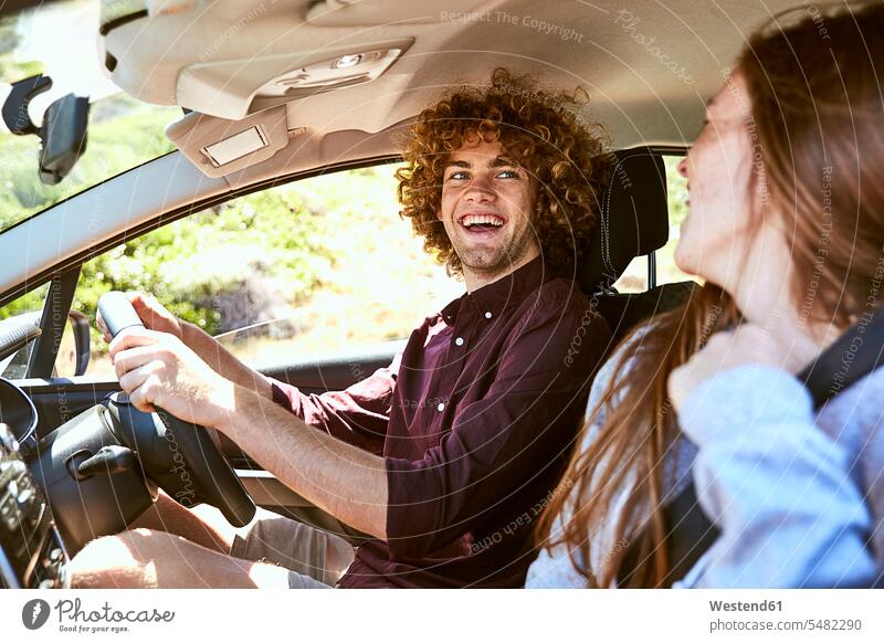 Lachender junger Mann, der Auto fährt und seine Freundin ansieht lachen Paar Pärchen Paare Partnerschaft fahren fahrend fahrender fahrendes Männer männlich