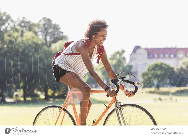 Lächelnde junge Frau fährt Fahrrad im Park fahren fahrend fahrender fahrendes Bikes Fahrräder Räder Rad weiblich Frauen Parkanlagen Parks lächeln Raeder