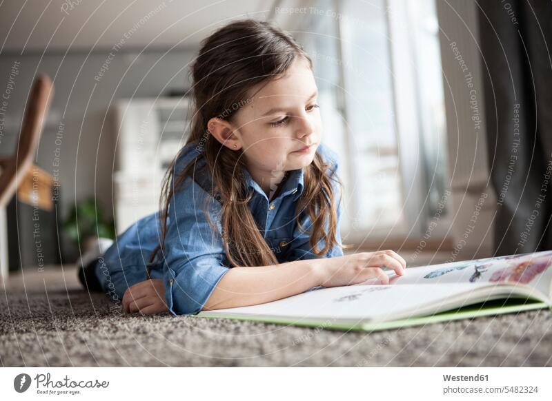 Porträt eines kleinen Mädchens, das auf dem Boden liegt und ein Bilderbuch betrachtet Deutschland Leser Lektüre Lektuere Bauchlage auf dem Bauch liegen Kindheit