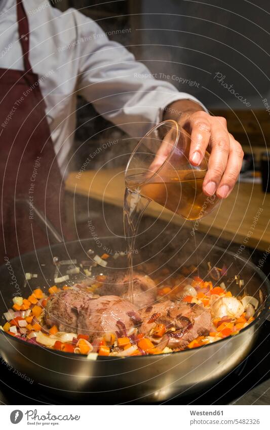 Mann gießt ein Glas Brandy in einer Pfanne mit sautiertem Gemüse auf Rinderbacken kochen Koch Küchenchefs Köche Koeche Kuechenchef Kuechenchefs Gastronomie
