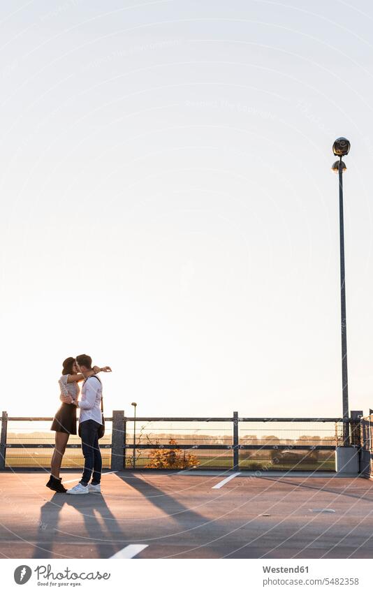 Junges Paar küsst sich bei Sonnenuntergang auf der Parkebene Parkdeck Parkdecks küssen Küsse Kuss Sonnenuntergänge Pärchen Paare Partnerschaft Parkhaus