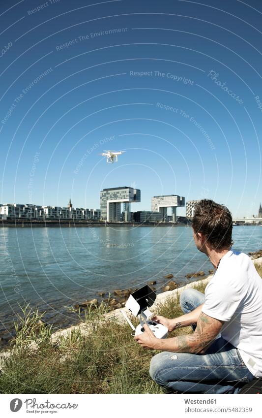 Reifer Mann sitzt im Gras und fliegt eine Drohne Drohnen steuern fotografieren fliegen fliegend sitzen sitzend filmen Männer männlich beobachten zuschauen