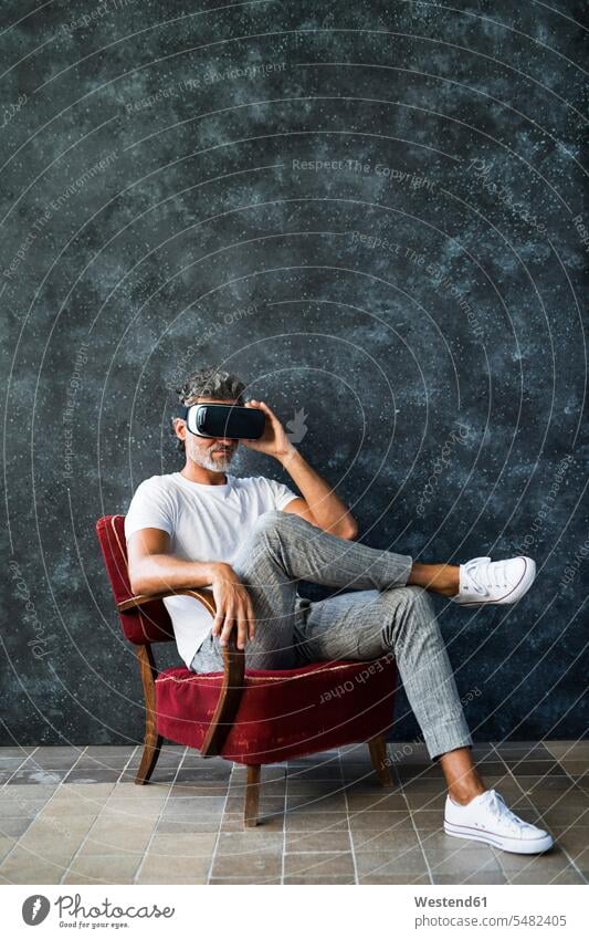 Reifer Mann, der durch eine VR-Brille schaut, im Sessel sitzend ansehen betrachten betrachtend Virtual Reality Brille Virtual-Reality-Brille