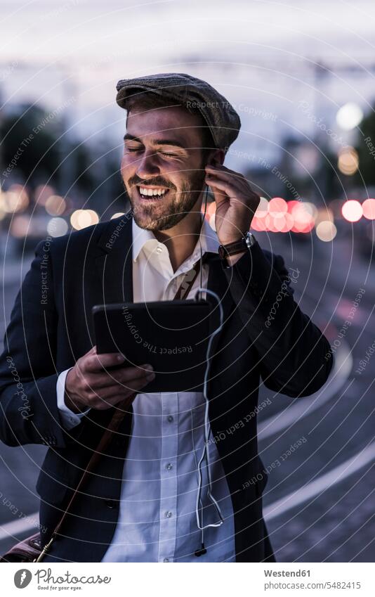 Glücklicher junger Mann in der Stadt mit Kopfhörern und Tablette in der Abenddämmerung lachen lächeln Männer männlich Tablet Computer Tablet-PC Tablet PC iPad
