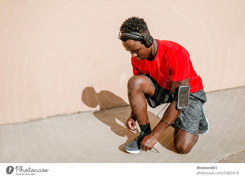 Mann in Sportkleidung bindet sich die Schuhe, während er mit Kopfhörern Musik hört Kopfhoerer Männer männlich Erwachsener erwachsen Mensch Menschen Leute People