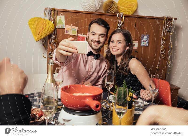 Freunde machen am Silvesterabend Selfies mit dem Smartphone Europäer Kaukasier Europäisch kaukasisch Selbstportrait sich selbst fotografieren Fonduetopf Topf