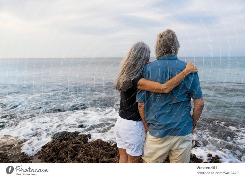 Älteres Ehepaar mit Blick auf das Meer, Rückansicht umarmen Umarmung Umarmungen Arm umlegen ansehen attraktiv schoen gut aussehend schön Attraktivität