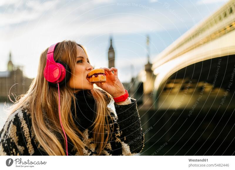 UK, London, junge Frau, die in der Nähe der Westminster Bridge Musik hört und einen Imbiss nimmt Städtereise City Trip Kurztripp City Break Himmel
