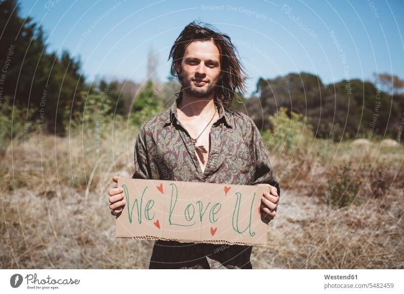 Hippie mit "We love you"-Schild in der Natur Europäer Kaukasier Europäisch kaukasisch Bart Bärte halten Außenaufnahme draußen im Freien Individualität