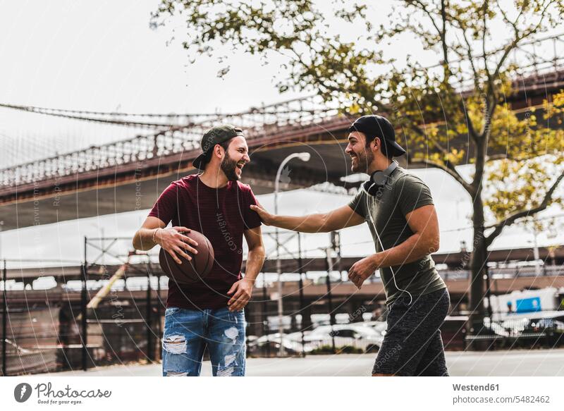 Zwei junge Männer mit Basketball amüsieren sich auf einem Aussenplatz Basketbaelle Basketbälle Mann männlich lachen spielen Spaß Spass Späße spassig Spässe